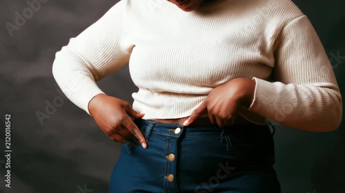 Plus size woman pointing at her waistline wearing blue denim jeans and white top, focus on body positivity and healthy lifestyle concept video