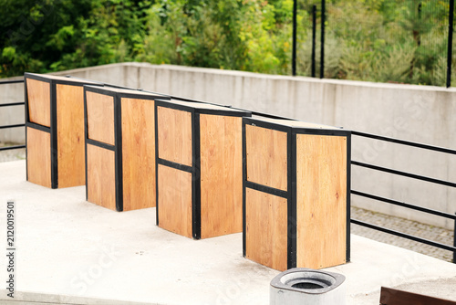 Row of outdoor wooden garbage bin enclosures with metal frames. Decorative trash container screens in modern residential complex courtyard.