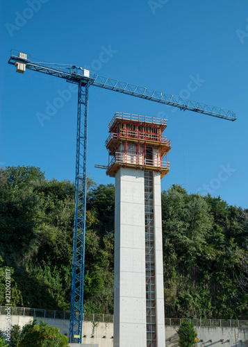 Construction site of high outdoor panoramic elevator tower with blue tower crane on a hill