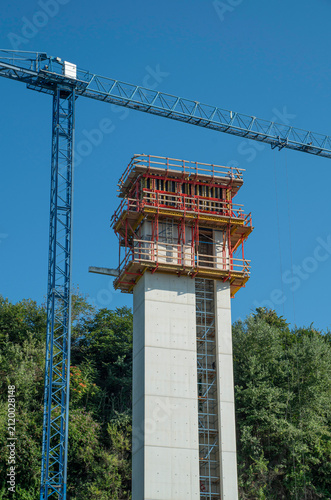 Construction site of high outdoor panoramic elevator tower with blue tower crane on a hill
