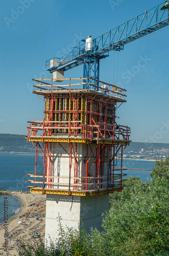 Construction of seaside outdoor lift tower with scaffoldings and crane overlooking beach