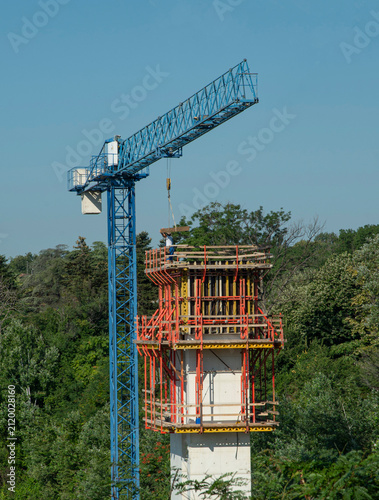Construction site of high outdoor panoramic elevator tower with blue tower crane on a hill