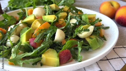 green salad with avocado mozzarella peach and arugula on white plate served on table showing fresh healthy cuisine concept of vegetarian recipes nutrition food styling and gastronomy