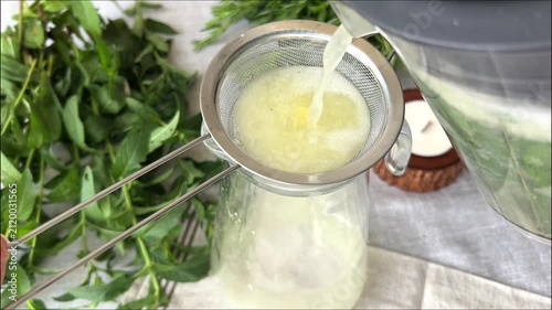 straining homemade summer lemonade through sieve with mint leaves and fresh ingredients showing beverage preparation process concept of healthy drinks cafes hospitality recipes and culinary content