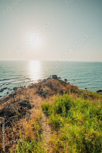 A narrow dirt path leading towards a rocky headland overlooking the gleaming sea at sunset