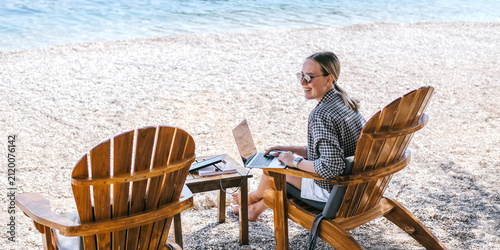 Foto Digital nomad working on laptop at beach lounge, portable solar panel charger on table, remote work vacation concept, sustainable travel, work from anywhere lifestyle