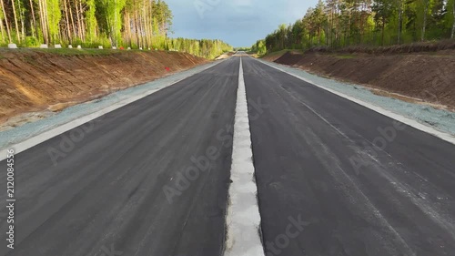A low, high-speed flight over a new two-lane paved road surrounded by forest on a sunny summer evening. Eastern Bypass, Novosibirsk, Russia.