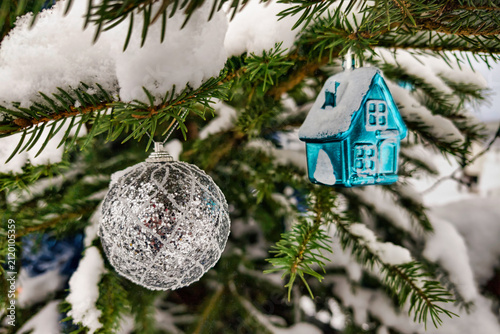 Christmas tree has silver and blue ornaments. Snow covers the tree branches in a winter landscape. This scene shows the holiday spirit during New Year time