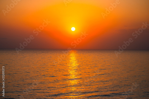 Obraz na plátně Wide angle shot of bright glowing sun setting over sea horizon casting golden light on calm water