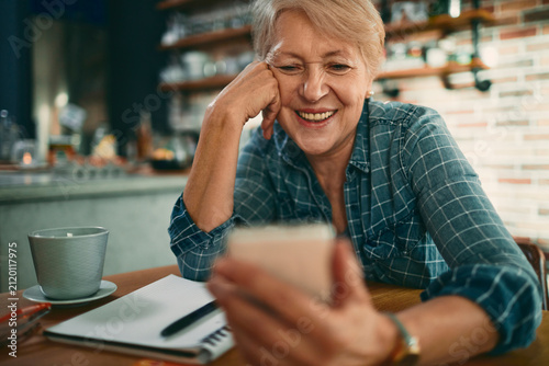 Smiling senior woman using smartphone in cafe