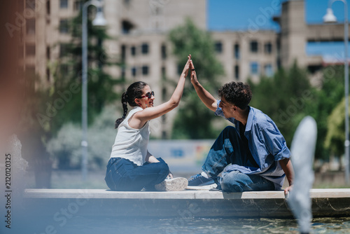 Foto Two young friends sit by a fountain and share a celebratory high five