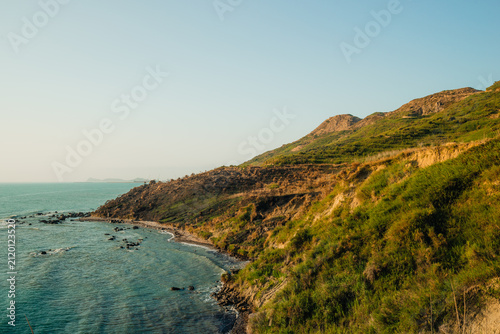 Foto Majestic green and brown coastal hills descending into a sparkling blue sea with