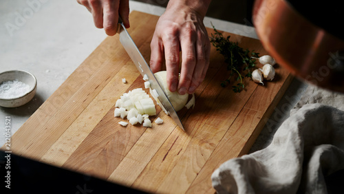 A chef chopping fresh onion on a wooden cutting board in a professional kitchen