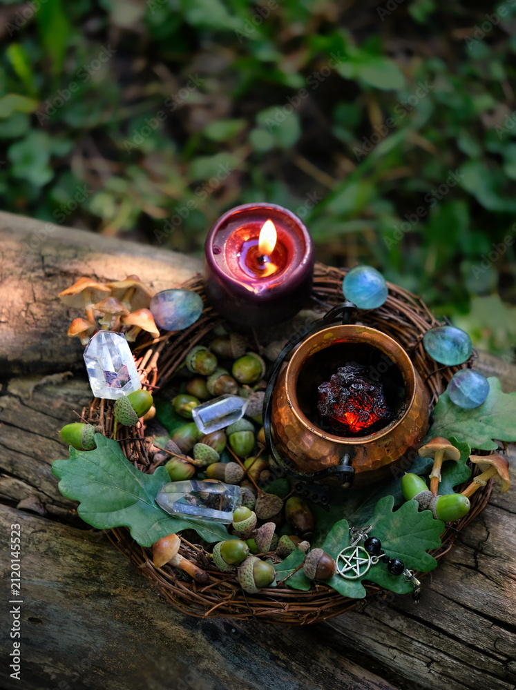 Fototapeta premium witch cauldron, black candle and crystals, acorns, oak leaves in forest, natural background. practical magic, occult ritual, witchcraft, esoteric spiritual ceremony. fairytale, mystery atmosphere