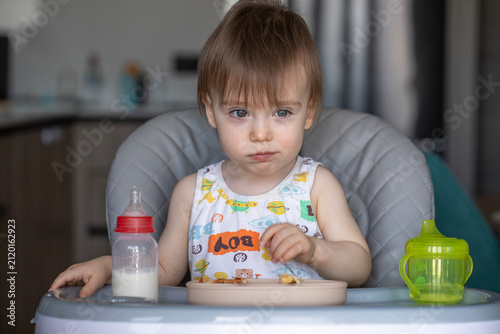 Infant girl eats deliciously while sitting at a childrens table