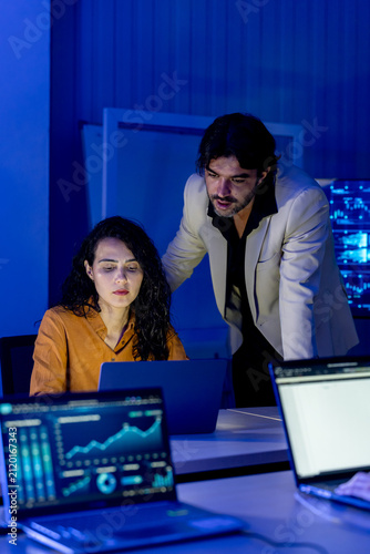 Adult male manager guides young female cybersecurity analyst during laptop review, with digital network dashboard supporting mentoring, threat analysis, secure workflow, and strategic decisions.
