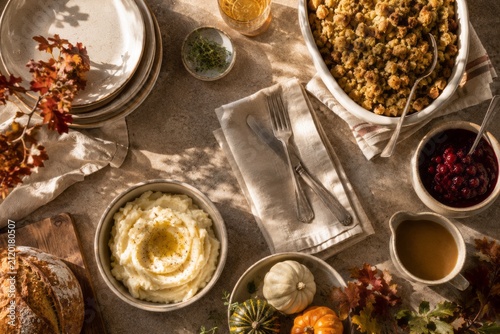 Thanksgiving dinner table with creamy mashed potatoes, stuffing, cranberry sauce, gravy and rustic bread. Cozy autumn holiday feast with seasonal decor and warm natural light.