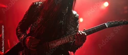 Heavy metal guitarist with long hair playing electric guitar on stage under dramatic red concert lighting