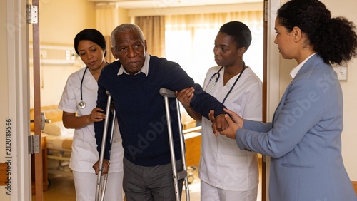 Rehabilitation nurses assisting elderly patient using crutches while promoting independence in nursing home.