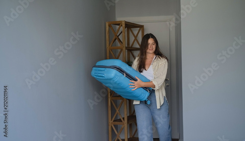 Woman bringing a blue suitcase to start packing for her trip, preparing clothes and beach essentials for a sunny vacation getaway.