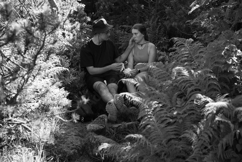 Konstfotografi Young couple resting in forest, sitting on rocks surrounded by ferns and foliage