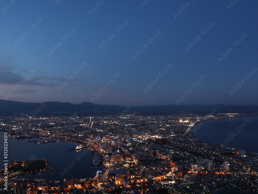 Fototapeta premium Coastal Cityscape at Dusk with Harbor Lights – Calm Sea Reflection and Mountain Silhouette in Evening Glow