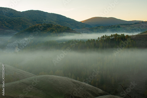 Fotografie Soft morning fog drifts through forested hills and rural valleys beneath a golden autumn sunrise
