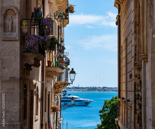 a glimpse of the blue Sicilian sea with a motorboat passing by, seen from the top of a narrow alley flanked by houses