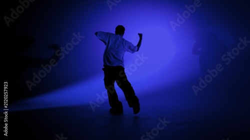 Hip hop dancer performing sharp arm movements in blue light