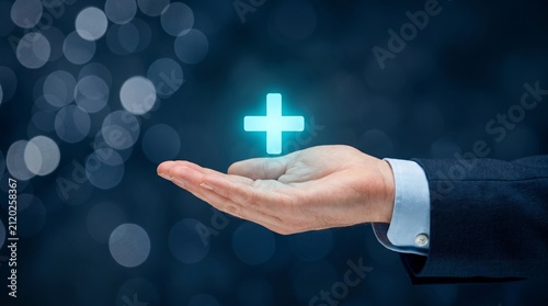 Glowing plus sign icon hovering over businessman hand, healthcare and medical insurance concept, positive growth and value added service