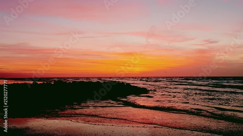Vibrant Pink and Orange Sunset Over the Ocean with Gentle Waves Lapping on a Rocky Shoreline. Cinematic and Serene Seascape.