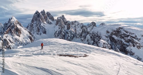 Cinematic orbital drone shot circling a backcountry skier crossing a snowy ridge in the Dolomites revealing dramatic alpine peaks pristine winter scenery and breathtaking mountain landscapes.