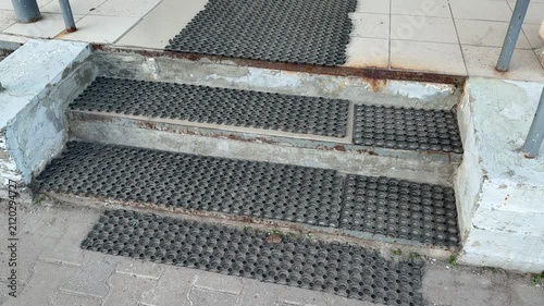 Rubber antiskid mats on rusty steps, closeup view of coarse tread and corroded metal edge at pickup point entrance, tiled landing