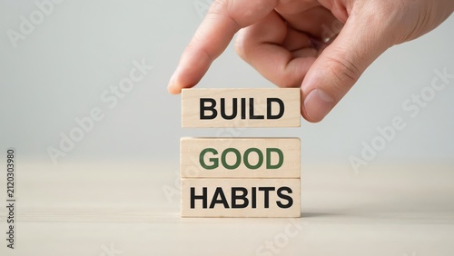 Hand stacking wooden blocks with Build Good Habits text on plain background