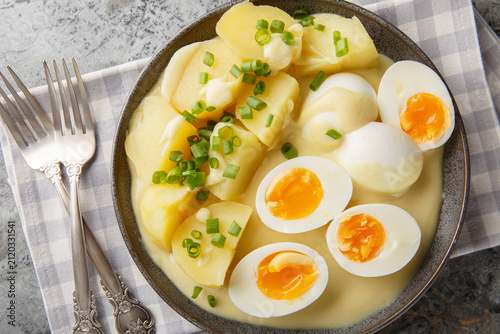 Photography Close-up of hard-boiled eggs in mustard sauce with a side dish of boiled potatoes in a plate on the table