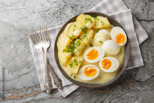 Senfeier hard boiled eggs in creamy mustard sauce with potato close-up in a plate on the table. Horizontal top view from above