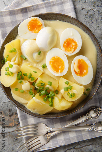 Senfeier German eggs in mustard sauce with a side dish of boiled potatoes close-up in a plate on the table. Vertical top view from above