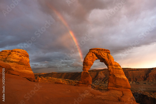 Rainbow and dark clouds behind Delicate Arch at Arches National Park, Utah