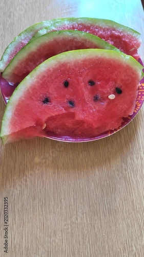 Stacked fresh watermelon slices with red flesh and black seeds on wooden surface, summer fruit.