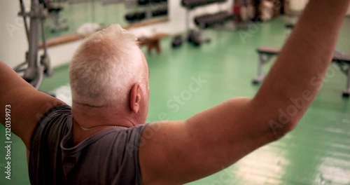 Middle-aged man performing lat pulldown, rear view.