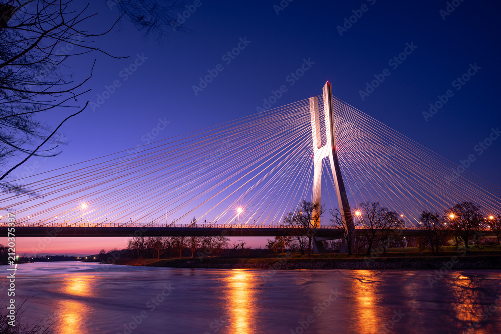 Fototapeta premium A modern cable-stayed bridge over the river, illuminated by lights.