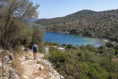 Hiker walking down a stony trail toward a secluded turquoise inlet. generative AI