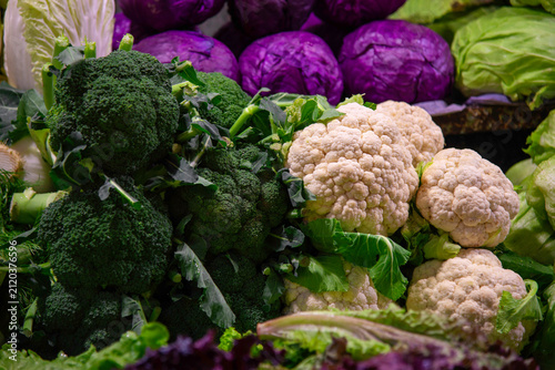 Fresh broccoli, cauliflower, and purple cabbage at market display.