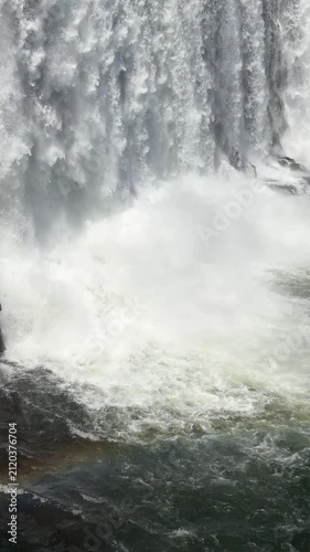 Close-up of a powerful waterfall cascading down into foaming turbulent water with mist and a faint rainbow
