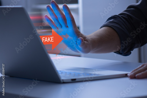 Person blocking fake information on a laptop with a stop gesture and digital warning overlay, illustrating misinformation prevention, fact checking, cybersecurity, and online content protection.