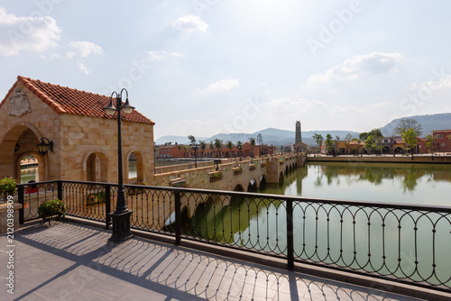 Fotografie European style stone arch bridge with black iron railings over a lake under brig