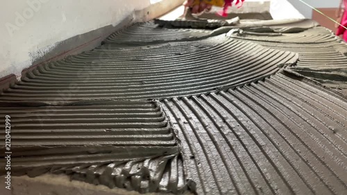 Wet cement adhesive spreads on the floor with notch trowel for tile installation.