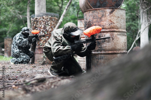 Paintball game outdoors with player in camouflage near old barrels