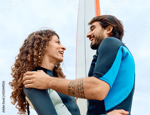 Photography Portrait of a young couple surfing at the beach, holding surfboards, having fun