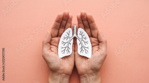 Hands protecting paper lung cutout on pink background representing respiratory health and awareness for medical science and wellness care